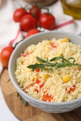 Tasty couscous with pepper, corn and arugula in bowl on white table, closeup