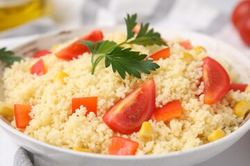 Tasty couscous with parsley, corn and tomatoes in bowl on table, closeup