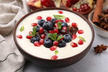 Delicious semolina pudding with blueberries, pomegranate, dates and mint in bowl on white table, closeup