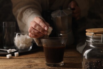 Fototapeta na wymiar Brewing aromatic coffee in moka pot. Woman putting sugar cubes in glass with drink at wooden table, closeup