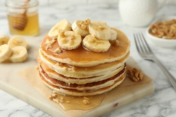 Delicious pancakes with bananas, walnuts and honey on white marble table, closeup