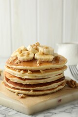 Delicious pancakes with bananas, walnuts and honey on white marble table