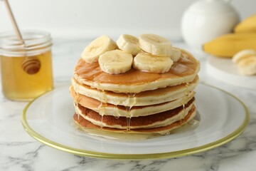 Delicious pancakes with bananas and honey on white marble table, closeup
