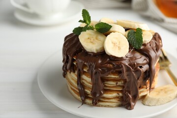 Tasty pancakes with chocolate spread, sliced banana and mint on white table, closeup. Space for text