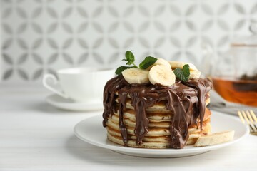 Tasty pancakes with chocolate spread, sliced banana and mint on white wooden table, space for text