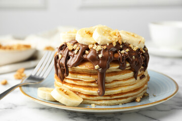 Tasty pancakes with chocolate spread, sliced banana and nuts served on table, closeup