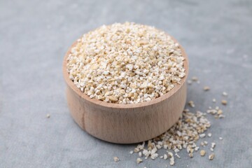 Raw barley groats in bowl on grey table, closeup