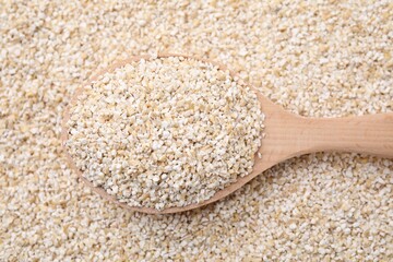 Wooden spoon on raw barley groats, top view