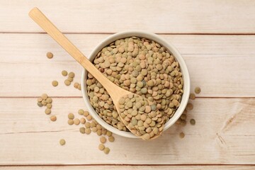 Raw lentils in bowl and spoon on light wooden table, top view