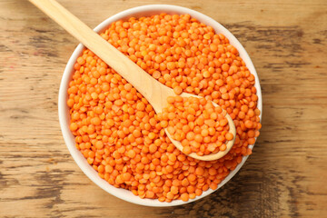 Raw red lentils in bowl and spoon on wooden table, top view