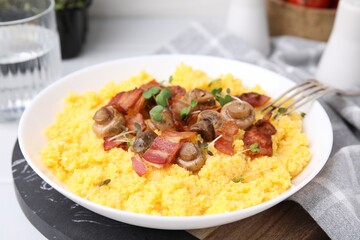Tasty cornmeal with bacon, mushrooms and microgreens in bowl on table, closeup