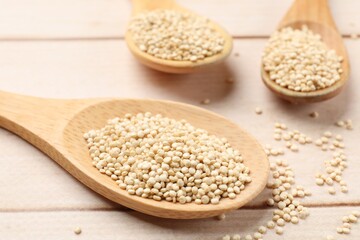 Spoons with raw quinoa on wooden table, closeup