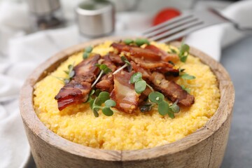 Cooked cornmeal with bacon and microgreens in bowl on light table, closeup