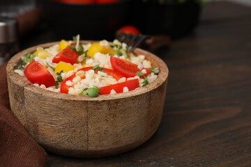 Cooked bulgur with vegetables in bowl on wooden table, closeup. Space for text