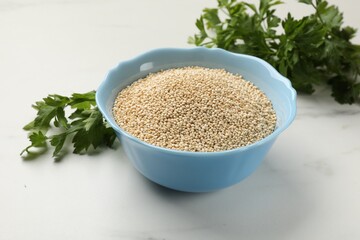 Dry quinoa seeds in bowl and parsley on white marble table