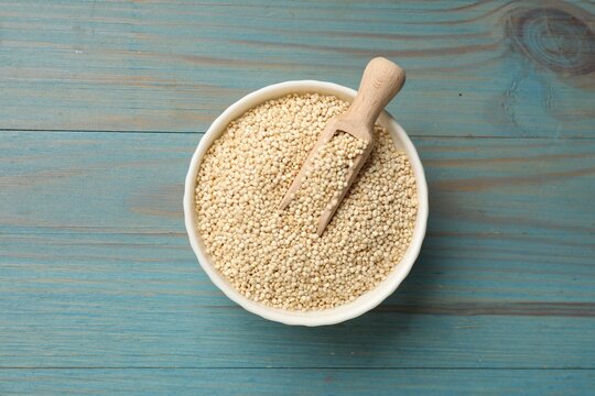Dry quinoa seeds and scoop in bowl on light blue wooden table, top view