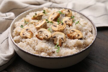 Delicious barley porridge with mushrooms and microgreens in bowl on table, closeup