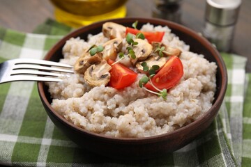Delicious barley porridge with mushrooms, tomatoes and microgreens in bowl served on table, closeup