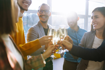 Business people celebrate with glasses of champagne in the office at a corporate event. A group of young people are having fun in the office. Holidays, business concept. - obrazy, fototapety, plakaty