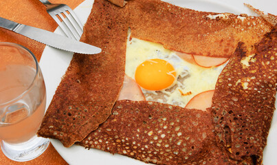 Galette complete. Traditional French buckwheat pancake with egg, cheese and ham served at typical Breton pancake restaurant (Creperie).