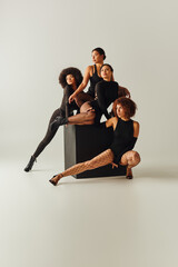 Obraz premium appealing african american women in sexy bodysuits posing together on black cube, fashion concept