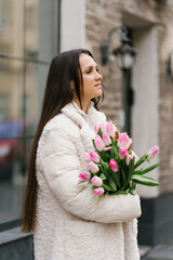 Beautiful woman are walking with a bouquet of tulips in a cities streets