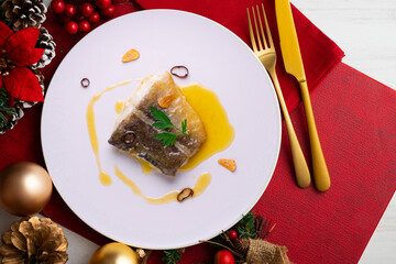 Bacalao al pil pil traditional tapa from north Spain. Codfish cooked with a delicious sauce made with oil, codfish and garlic. Christmas food served on a table decorated with Christmas motifs.