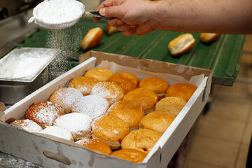 A baker sprinkles sugar powder on Hanukkah donuts in a bakery.