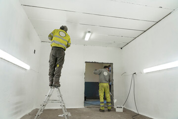 Two Skilled Workers in Overalls Transform a Spacious Room or Garage with Paint.