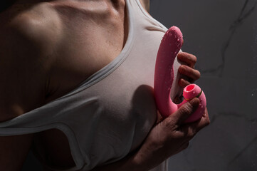A woman in a white tank top stands in the shower and holds a curved pink sex toy. 