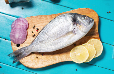 Raw dorado fish on cutting board on blue wooden table with ingredients for cooking