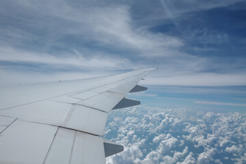 Beautiful clear deep blue sky over thick layer of clouds at stratosphere atmosphere viewed from airplane's window located above airplane's wing and jet.