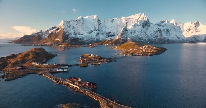 Aerial view of rocks in snow, islands with rorbuer, sea, bridge, mountains, road, blue sky at sunrise in winter. Beautiful top drone view of Hamnoy and Reine village, Lofoten islands, Norway. Travel