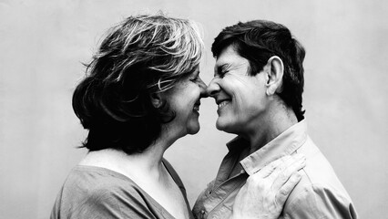Senior gay lesbian couple kissing outside. LGBTQ aged lovers having tender moment. Black and white editing - obrazy, fototapety, plakaty