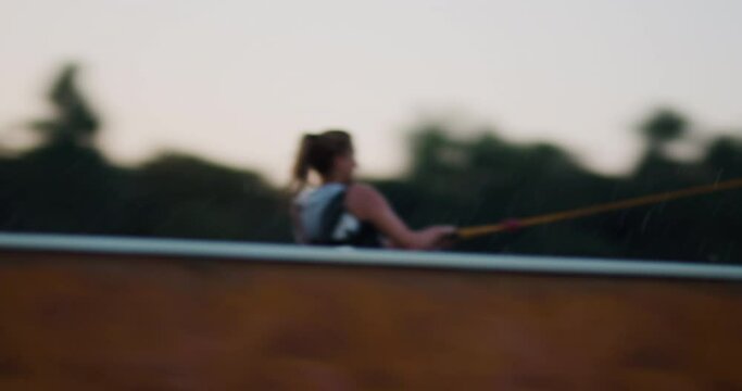 Female wakeboarder wakesurfing at sunset. Girl riding on waterski cable. Holding tow rope. Summer activities in a lake.