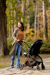 Young woman with cute baby girl in baby stroller at the autumn park