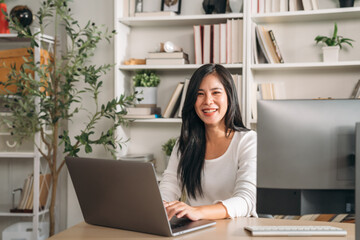 Beautiful young woman using laptop while working in home office. Businesswoman happy and smiling at indoors.