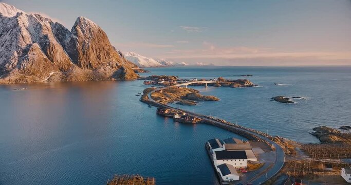 Aerial view of rocks in snow, islands with rorbuer, sea, bridge, mountains, road, blue sky at sunrise in winter. Beautiful top drone view of Hamnoy and Reine village, Lofoten islands, Norway. Travel