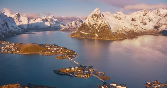 Aerial view of snowy rocks, islands with rorbuer, sea bay, bridge, mountains, road, pink sky at sunrise in winter. Beautiful top drone view of Hamnoy and Reine village, Lofoten islands, Norway. Nature