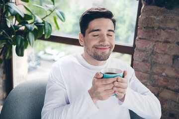 Photo of dreamy funky young guy wear white shirt closed eyes enjoying cacao flavor aroma indoors apartment room