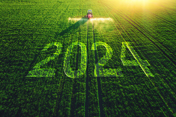 2024 Happy New Year concept and Aerial view of farming tractor plowing and spraying on field.