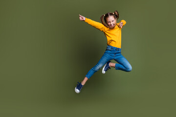 Full length photo of funny kid with ponytails hairdo dressed yellow shirt flying kicking empty space isolated on khaki color background