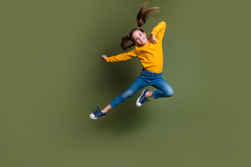 Fototapeta na wymiar Full length photo of adorable kid with ponytails hairdo dressed yellow shirt flying in empty space isolated on khaki color background