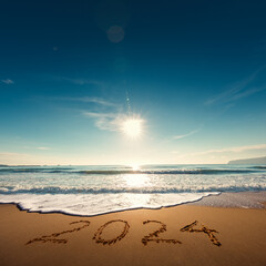 Beautiful sunrise over the sea. Happy New Year 2024 written on seashore.