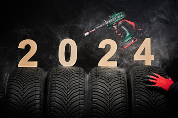 2024 happy new year, winter care tires and hands of a man with screwdriver for wheels on black...