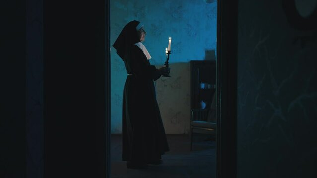 Spirit of a nun walking slowly with burning candles in a haunted house at night