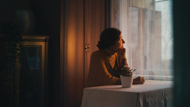 Thoughtful granny sitting at table, remembering past, looking out the window