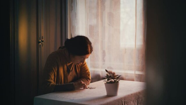 Sad senior woman counting coins on table, low pension and poverty problem