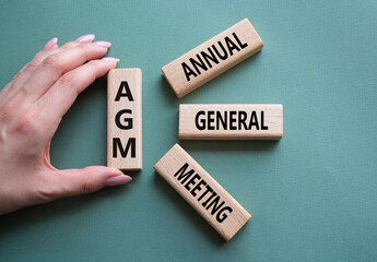 AGM - Annual general meeting symbol. Concept word AGM on wooden blocks. Businessman hand. Beautiful...