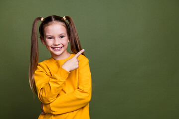 Photo of good mood schoolgirl with ponytails wear yellow pullover indicating at offer empty space...